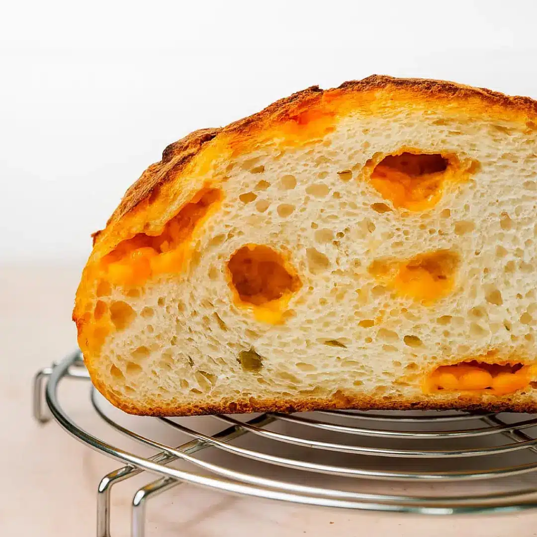 jalapeno-cheddar-sourdough-slice Close-up of a sliced jalapeno cheddar sourdough loaf on a cooling rack.